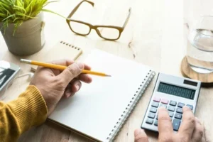 A person using a calculator and notepad to track costs.